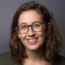 Headshot photograph: woman wearing glasses with light brown and wavy hair.