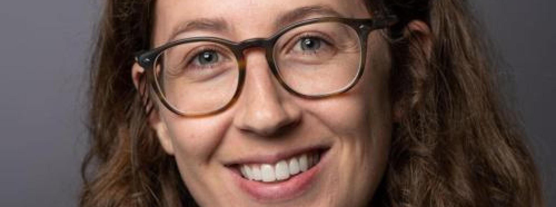 Headshot photograph: woman wearing glasses with light brown and wavy hair.