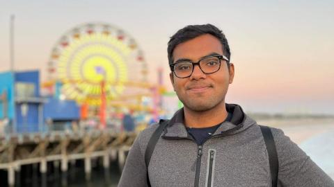 A man smiling with a scenic ocean behind him and a ferris wheel