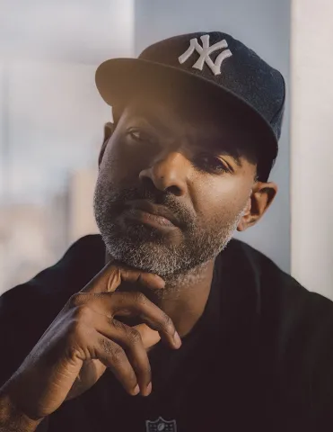 African-American man in a navy blue New York cap, with his hand under his chin.