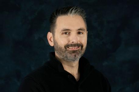 Headshot photograph of Chris Mattman with dark background behind him