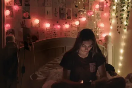 Girl sitting on bed on her laptop with twinkle lights behind her