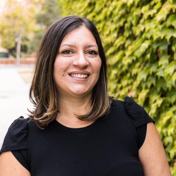 Melissa Villa Nicholas smiling in front of wall of foliage. 
