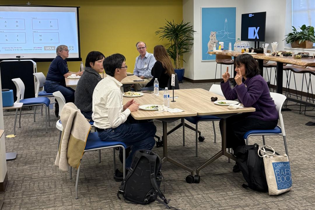Professors gathered around small tables; having conversations with each other.